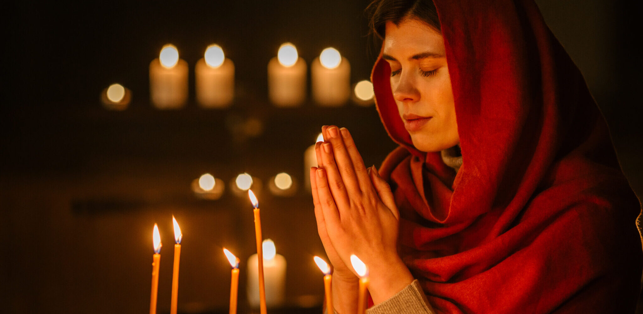 Devout Christian Woman with Head Scarf Lighting a Candle in Church, Praying and Expressing Devotion to Lord. Female Parishioner hoping and Wishing with Closed Eyes keeping her heart Pure with Prayers